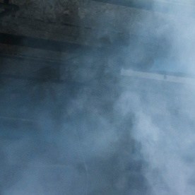 Dodge Charger blanco realizando burnout con humo de neumáticos en entorno industrial, vista trasera lateral del potente muscle car