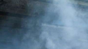 Dodge Charger blanco realizando burnout con humo de neumáticos en entorno industrial, vista trasera lateral del potente muscle car