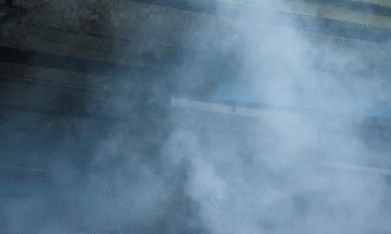Dodge Charger blanco realizando burnout con humo de neumáticos en entorno industrial, vista trasera lateral del potente muscle car