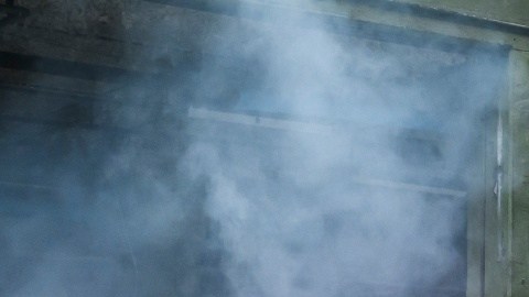 Dodge Charger blanco realizando burnout con humo de neumáticos en entorno industrial, vista trasera lateral del potente muscle car