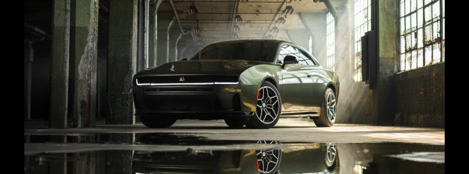 Dodge Charger verde oliva en almacén abandonado con reflejos en el suelo, fotografía dramática del muscle car americano