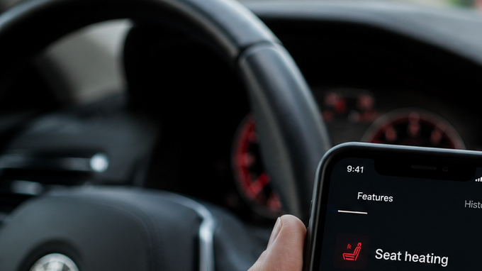 App de BMW en smartphone mostrando suscripción de calefacción de asientos por $18 mensuales desde el interior del vehículo