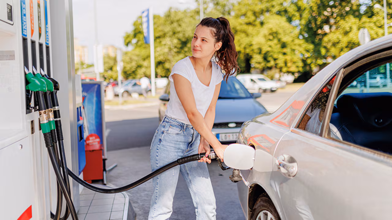Mujer joven llena el tanque de su coche en gasolinera durante día soleado
