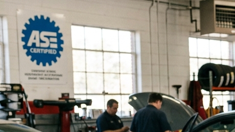Mecánico certificado ASE explica reporte de salud vehicular a cliente en taller de reparación de autos