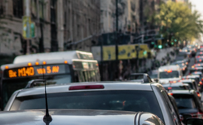 Embotellamiento en calle urbana con fila de vehículos, autobuses y luces de freno encendidas en hora punta.