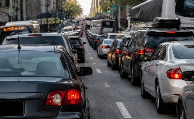 Embotellamiento en calle urbana con fila de vehículos, autobuses y luces de freno encendidas en hora punta.
