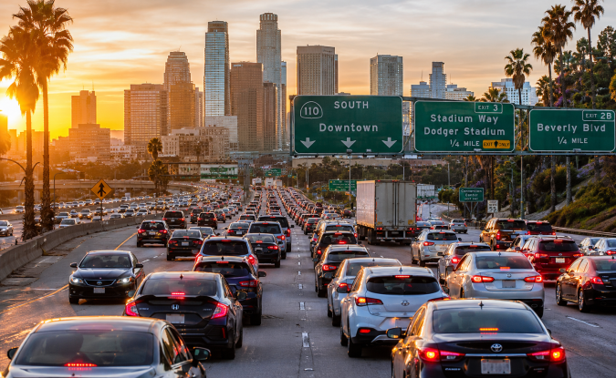 Atasco masivo en la 110 South Los Ángeles al atardecer, tráfico intenso con palmeras y rascacielos de downtown