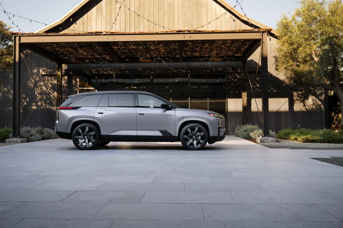 Vista lateral del Toyota Highlander Limited 2027 en acabado Spellbound 2Tone, estacionado bajo pérgola rústica moderna. Diseño elegante SUV híbrido.