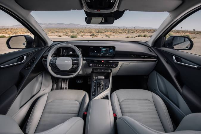 Interior del Kia Niro 2027 con asientos claros, tablero digital y vista panorámica al desierto.