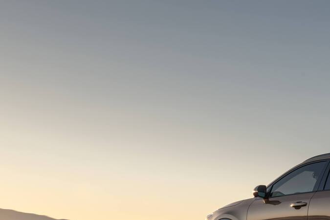 Vista trasera tres cuartos del Kia Niro 2027 en movimiento por carretera al atardecer, aspecto deportivo.
