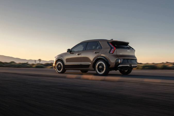 Vista trasera tres cuartos del Kia Niro 2027 en movimiento por carretera al atardecer, aspecto deportivo.
