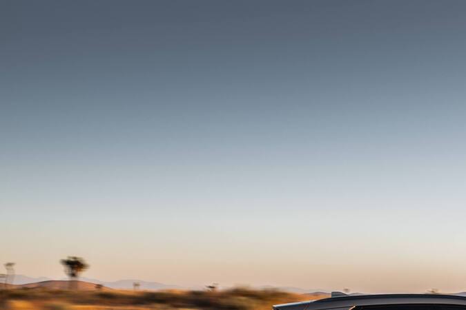 Kia Niro 2027 gris circulando a alta velocidad en carretera desértica al atardecer, vista lateral dinámica.