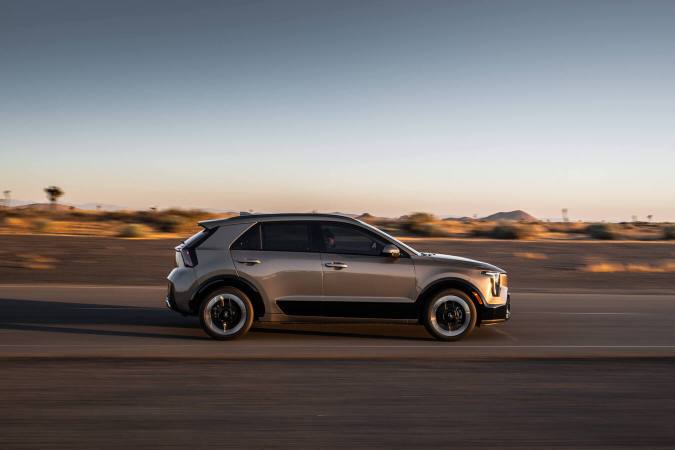 Kia Niro 2027 gris circulando a alta velocidad en carretera desértica al atardecer, vista lateral dinámica.