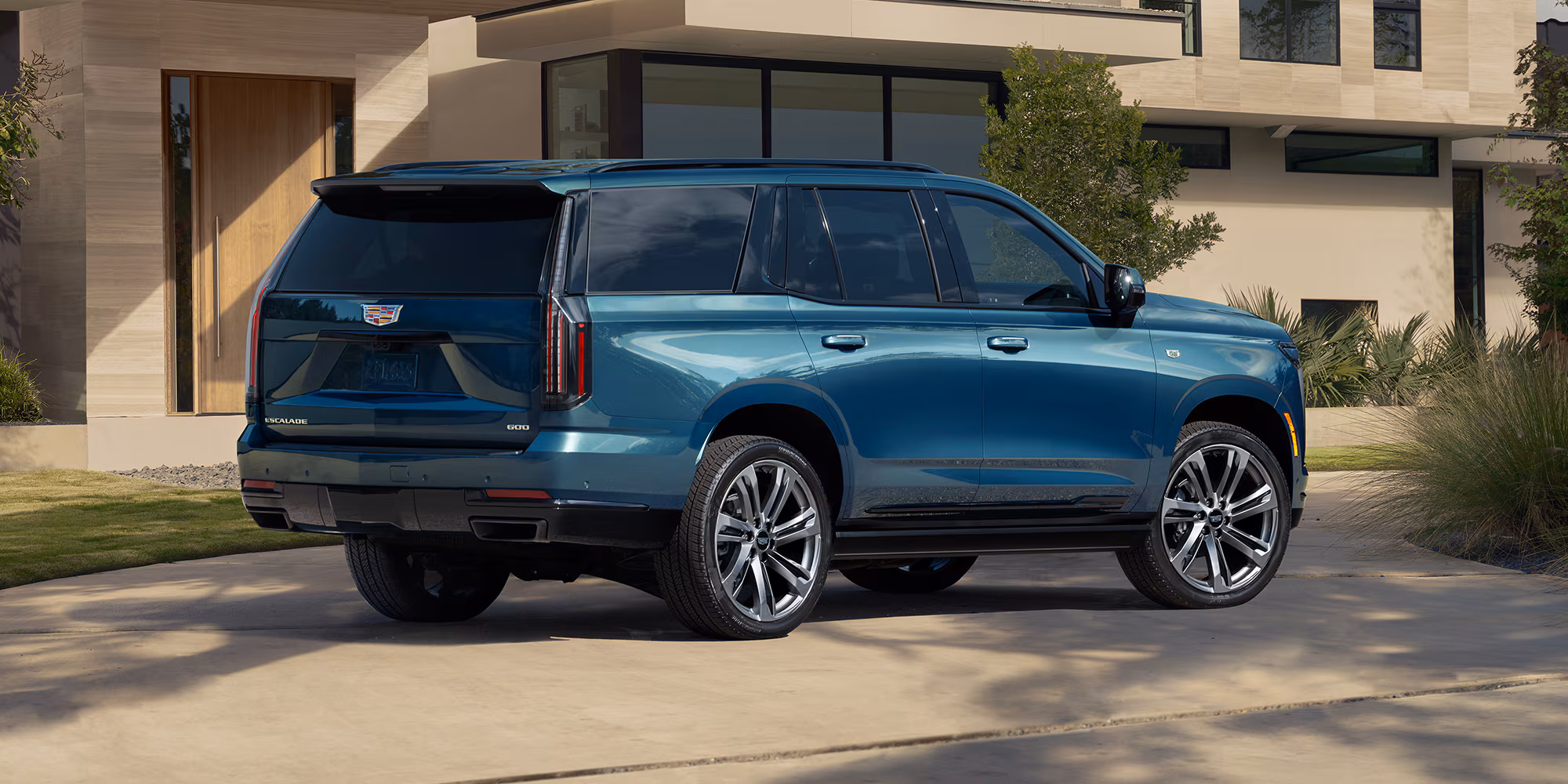 Cadillac Escalade 2026 azul aparcado frente a casa moderna, SUV de lujo grande con diseño robusto y estilo premium.