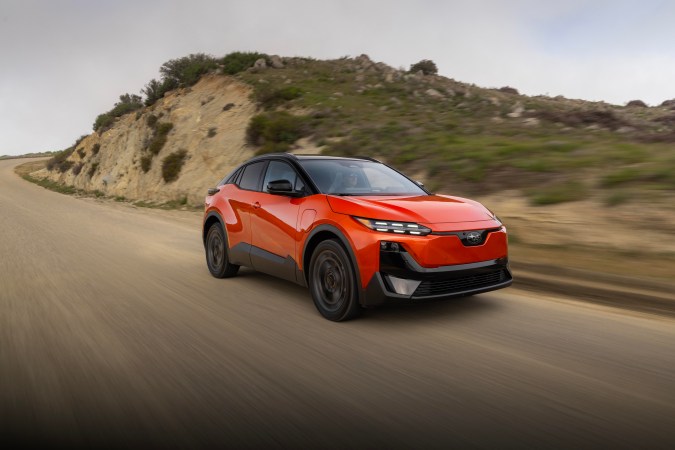 Subaru Uncharted 2027 naranja en carretera de montaña, SUV coupé eléctrico deportivo en plena conducción a alta velocidad.