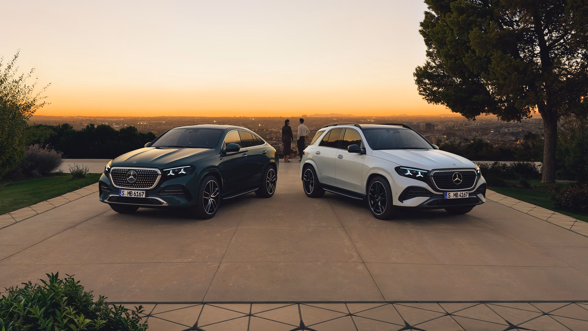 Mercedes‑Benz GLE Coupé y GLE SUV estacionados al atardecer con vista panorámica de ciudad, SUVs de lujo con presencia imponente.”