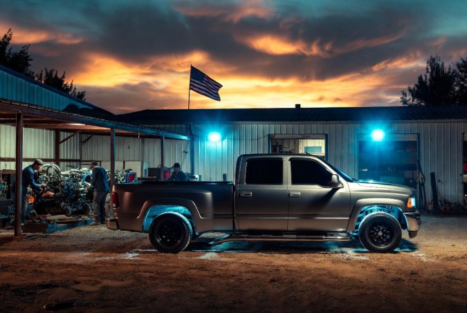 Pickup truck tuner customizada frente a taller mecánico al atardecer con bandera americana.