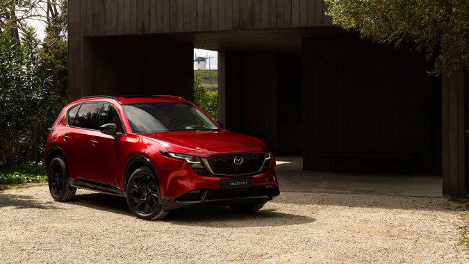 Mazda CX-5 2026 rojo estacionado frente a una vivienda moderna, mostrando su diseño exterior y parrilla frontal.
