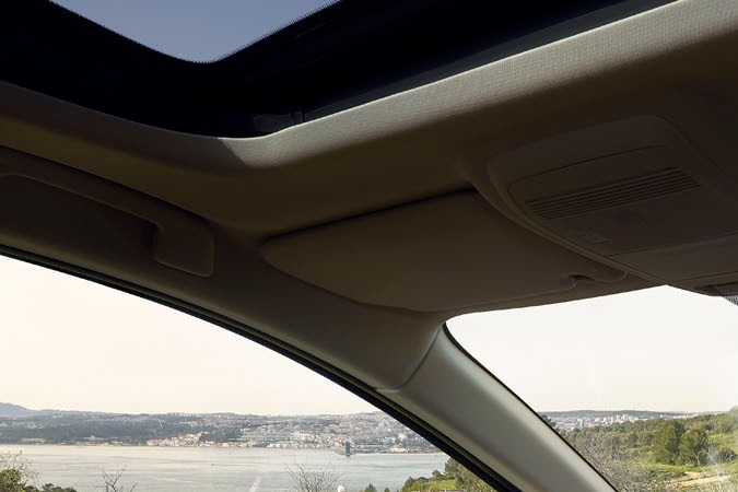 Interior del Mazda CX-5 2026 con pantalla multimedia, tablero digital, techo panorámico y paisaje costero visible.