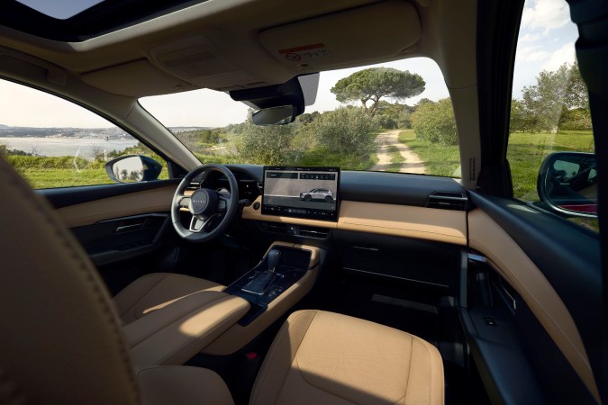 Interior del Mazda CX-5 2026 con pantalla multimedia, tablero digital, techo panorámico y paisaje costero visible.