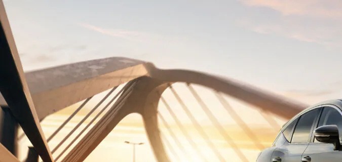 Nissan Murano 2027 color champán circulando sobre un puente al atardecer.