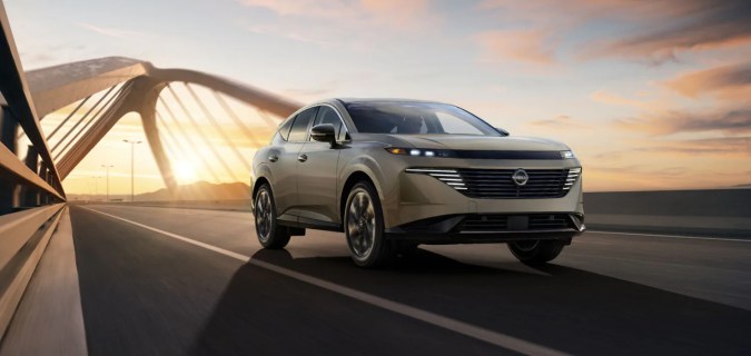 Nissan Murano 2027 color champán circulando sobre un puente al atardecer.