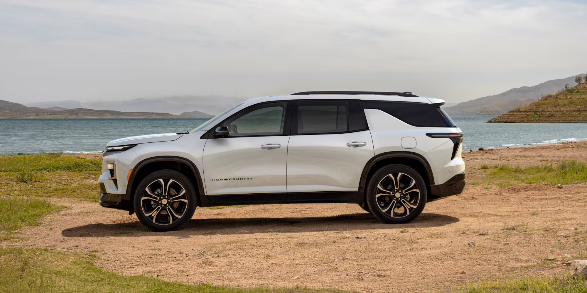 2027 Chevrolet Traverse High Country blanca estacionada frente a un lago y paisaje montañoso.