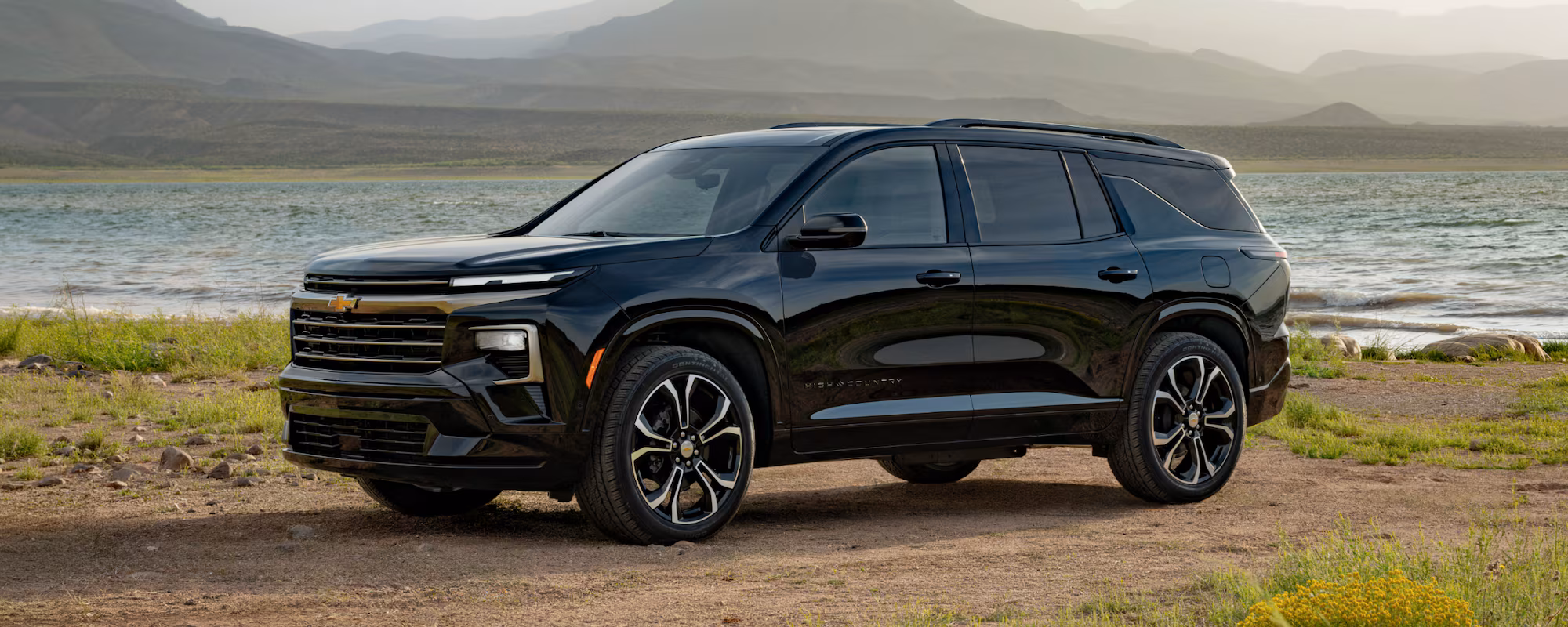2027 Chevrolet Traverse High Country negra junto a un lago y montañas.