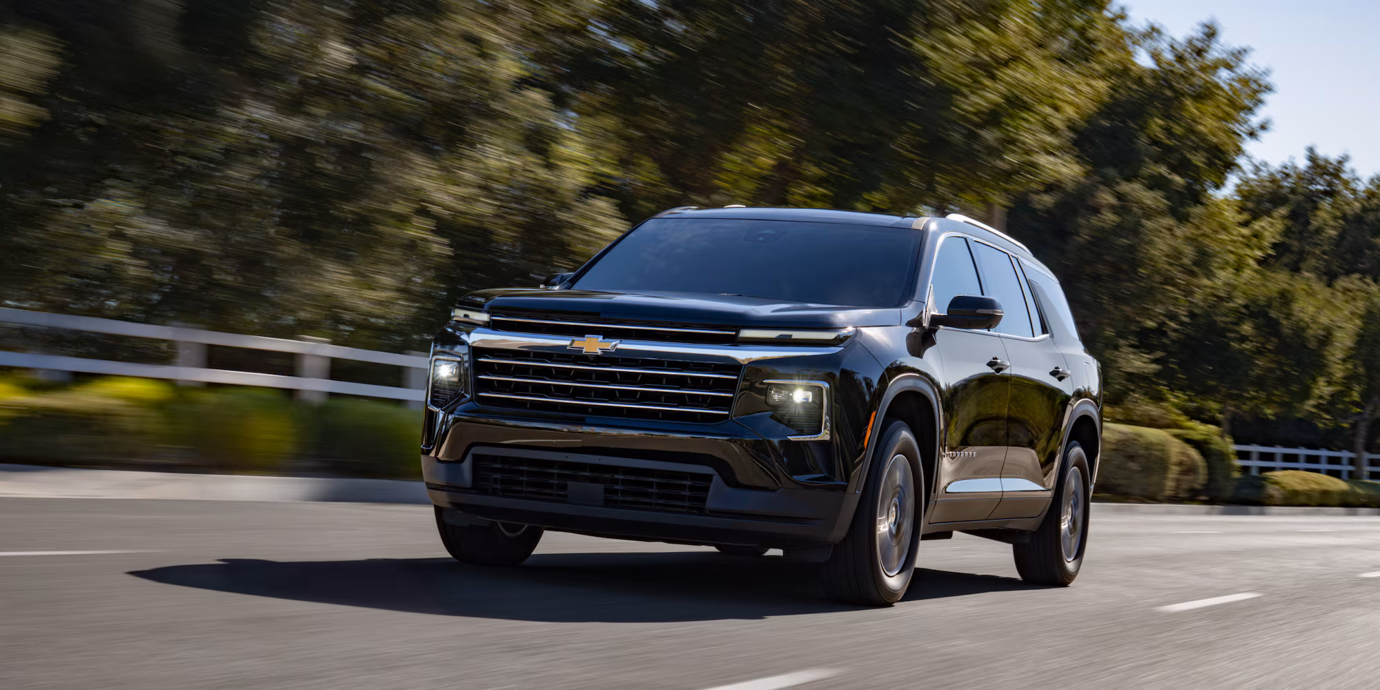 2027 Chevrolet Traverse High Country negra circulando por una carretera arbolada.