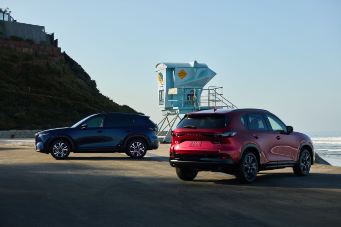 Versiones de la Mazda CX-5 2026 junto a una playa, con una torre de salvavidas y el océano al fondo.