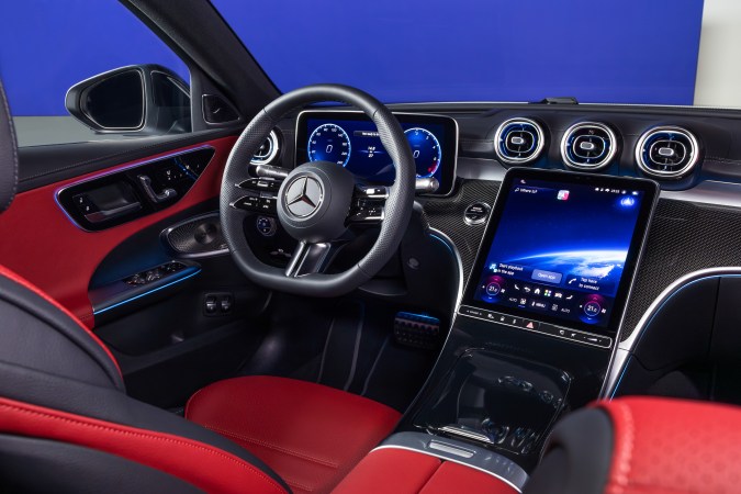Interior del Mercedes-Benz Clase C con volante multifunción, pantalla central MBUX y tapicería deportiva en color rojo.