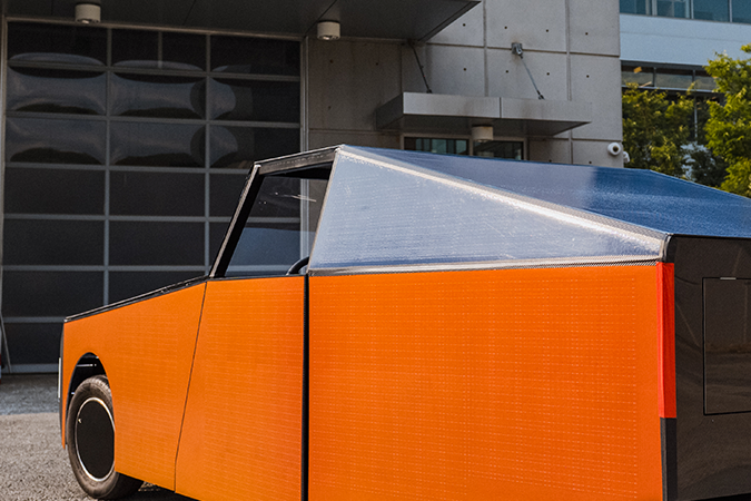 Luminetta DO17 naranja vista desde atrás, con diseño futurista y carrocería eléctrica compacta frente a un edificio moderno.