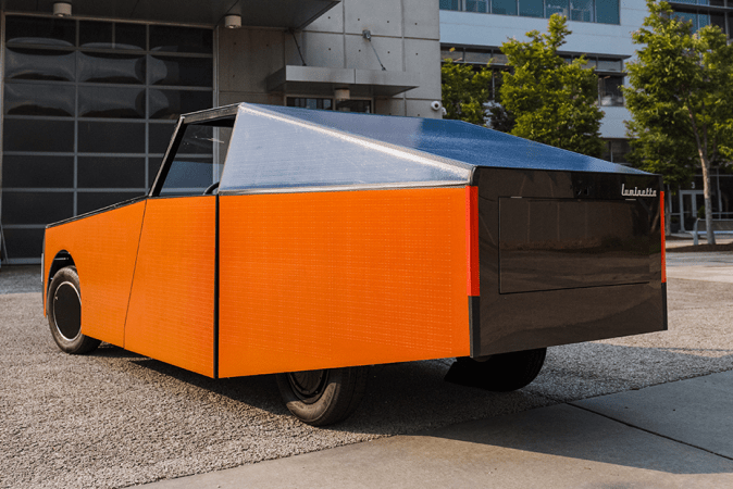 Luminetta DO17 naranja vista desde atrás, con diseño futurista y carrocería eléctrica compacta frente a un edificio moderno.