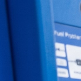 Surtidor de gasolina con precios de combustible regular, extra y premium junto a un vehículo durante el repostaje.