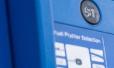 Surtidor de gasolina con precios de combustible regular, extra y premium junto a un vehículo durante el repostaje.