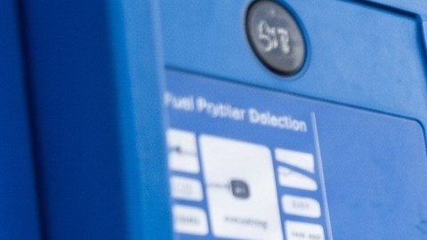 Surtidor de gasolina con precios de combustible regular, extra y premium junto a un vehículo durante el repostaje.