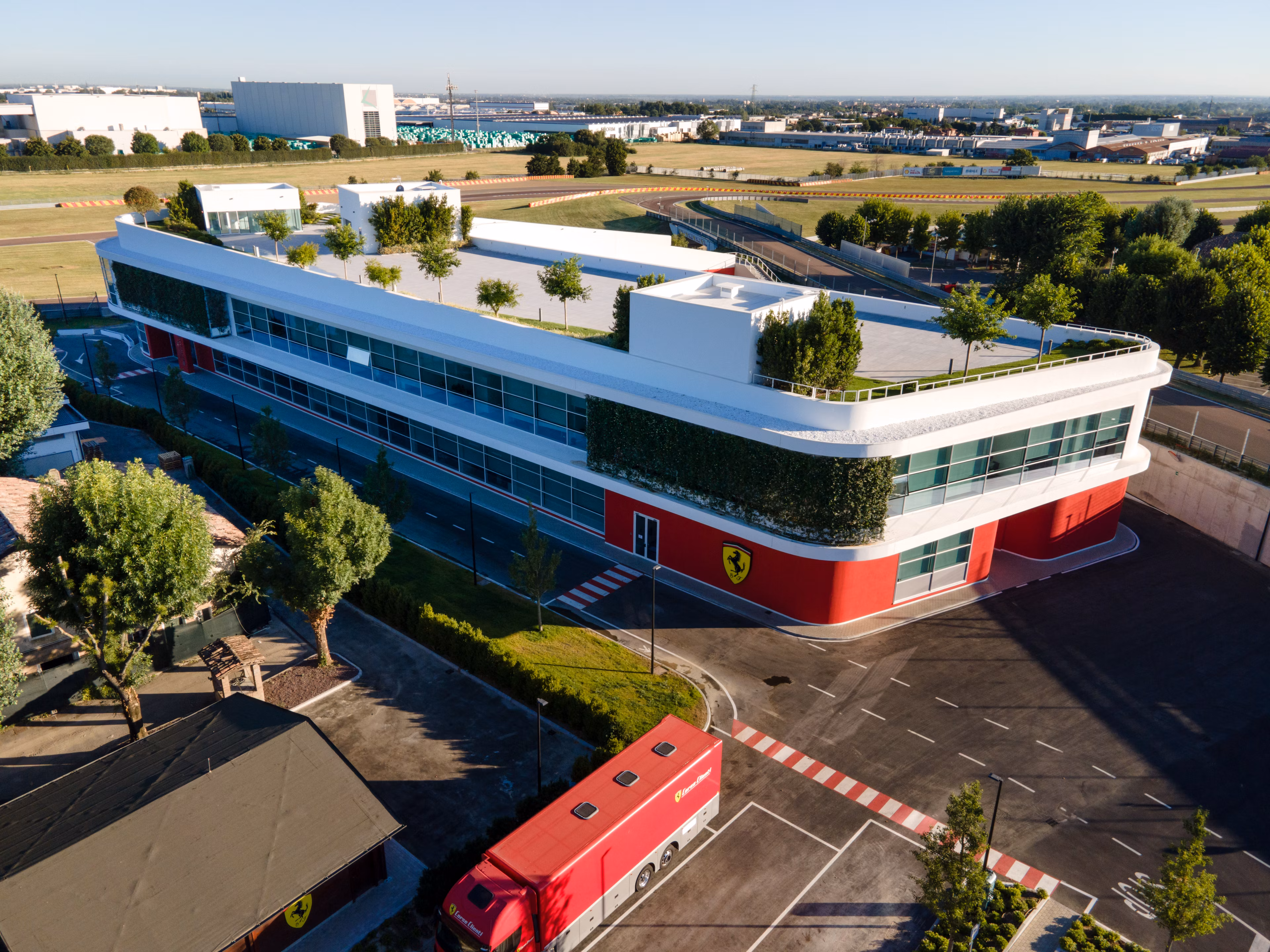 Vista aérea del moderno edificio de Ferrari con detalles en rojo y un camión de la marca estacionado en las instalaciones.