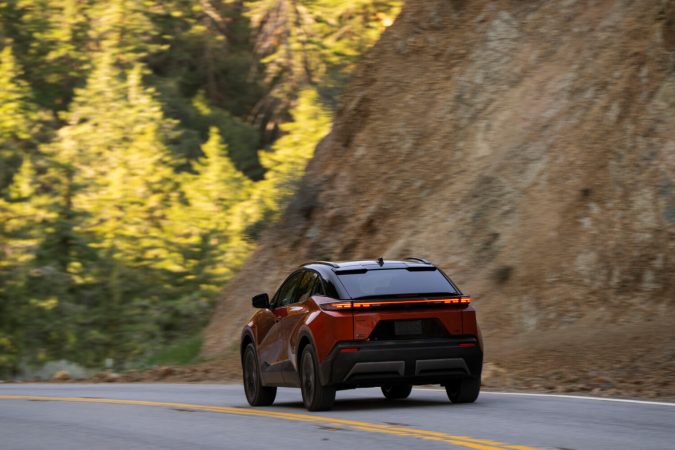 Toyota C-HR 2026 rojo circulando por una carretera montañosa rodeada de árboles y naturaleza.