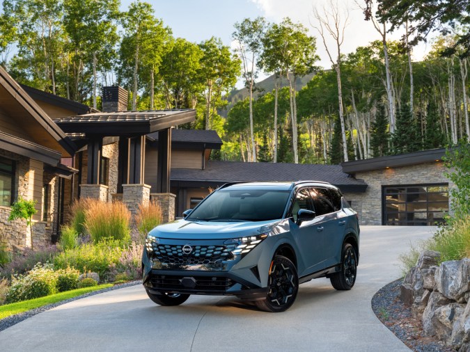 Camioneta SUV Nissan Rogue Hybrid azul estacionada en la entrada de una casa moderna de montaña.