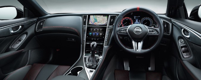 Interior deportivo del Nissan Skyline NISMO con volante multifunción, acabados en fibra de carbono y detalles en costura roja.