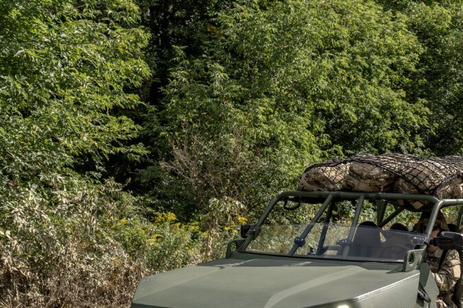 Vehículos Infantry Squad Vehicle verdes de GM Defense circulando por terreno fangoso en bosque.
