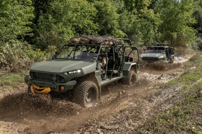 Vehículos Infantry Squad Vehicle verdes de GM Defense circulando por terreno fangoso en bosque.