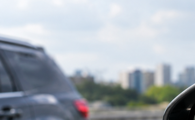 Espejo retrovisor lateral de auto con la alerta de punto ciego ADAS iluminada, advirtiendo sobre un vehículo cercano en la autopista.