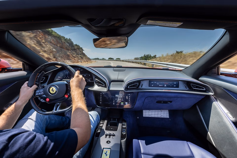 Interior de Ferrari Roma Spider en carretera panorámica, mostrando volante deportivo, tablero digital y acabados de lujo.