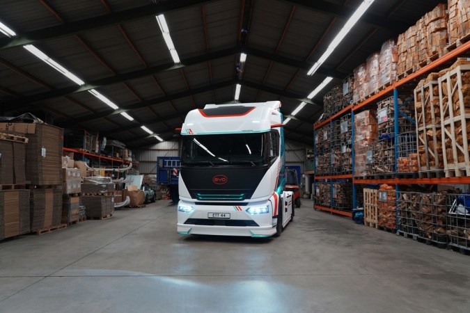 Camión eléctrico BYD ETT 44 con luces encendidas dentro de almacén logístico con estanterías de mercancía.
