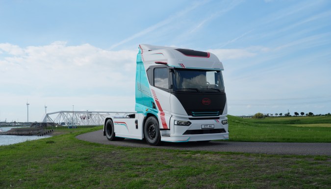 Camión eléctrico BYD ETT 44 blanco y turquesa circulando por carretera junto a puente y paisaje verde.