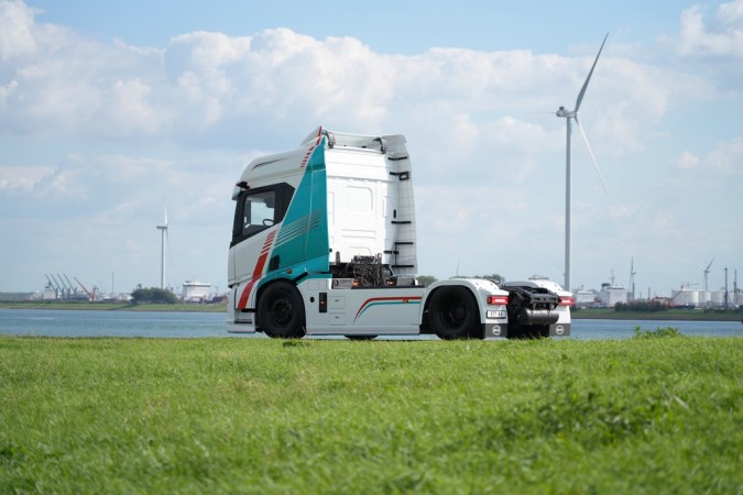 Vista lateral del camión eléctrico BYD ETT 44 blanco junto a río y aerogeneradores en día soleado.