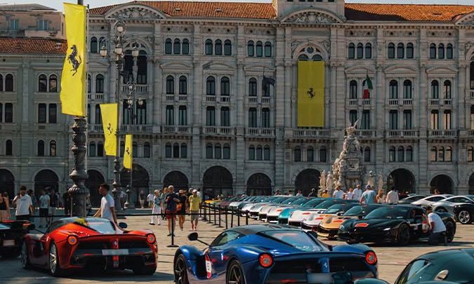 Exclusiva exhibición de múltiples autos deportivos Ferrari de diferentes colores estacionados en una plaza histórica frente a un imponente edificio monumental en Italia.