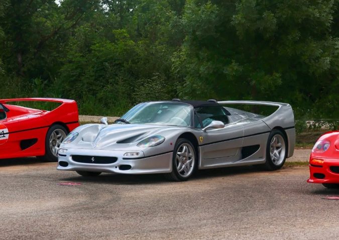 Espectacular auto deportivo clásico Ferrari F50 color gris plata estacionado al aire libre, acompañado de otros icónicos modelos Ferrari rojos.