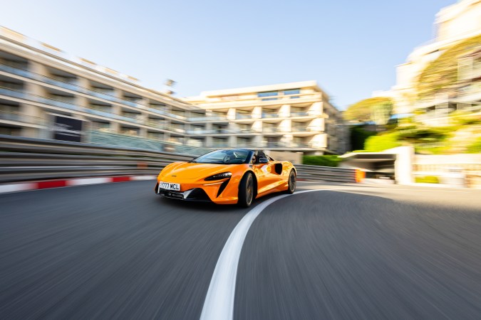 McLaren Artura Spider naranja en pista de Monaco con edificios de fondo y efecto de movimiento.